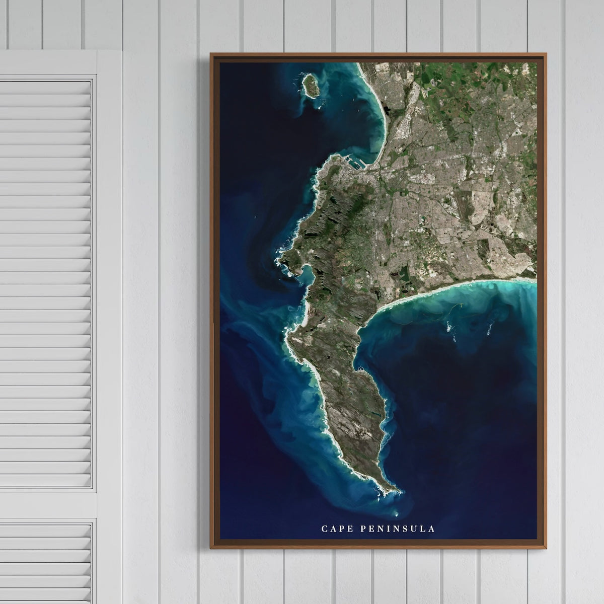 Cape Peninsula satellite print in a dark wood frame on a white panelled wall, showing the peninsula from Table Bay to Cape Point with the title Cape Peninsula on the image.