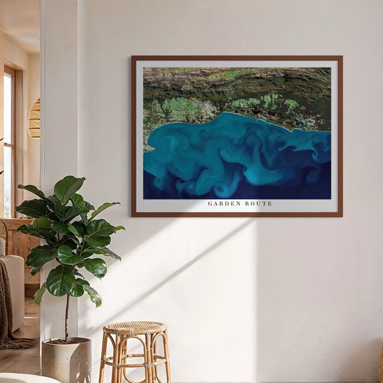 Garden Route 1 satellite poster print framed on a neutral wall above a rattan stool, with swirling ocean currents and the title Garden Route on the bottom white border.