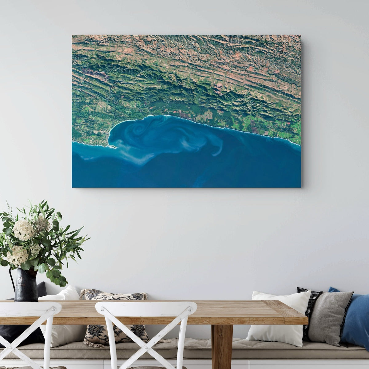 Garden Route 2 East satellite print hung on a white wall above a dining table, showing deep blue ocean currents against the green coastal mountains.