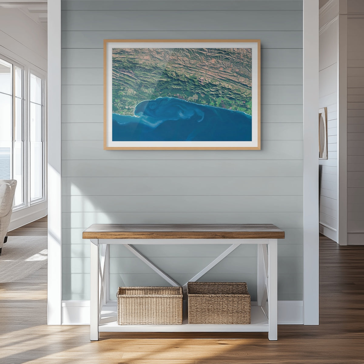 Garden Route 2 East satellite print in a light oak frame above a console table, showing deep blue water and ocean currents along the green coastal mountains.