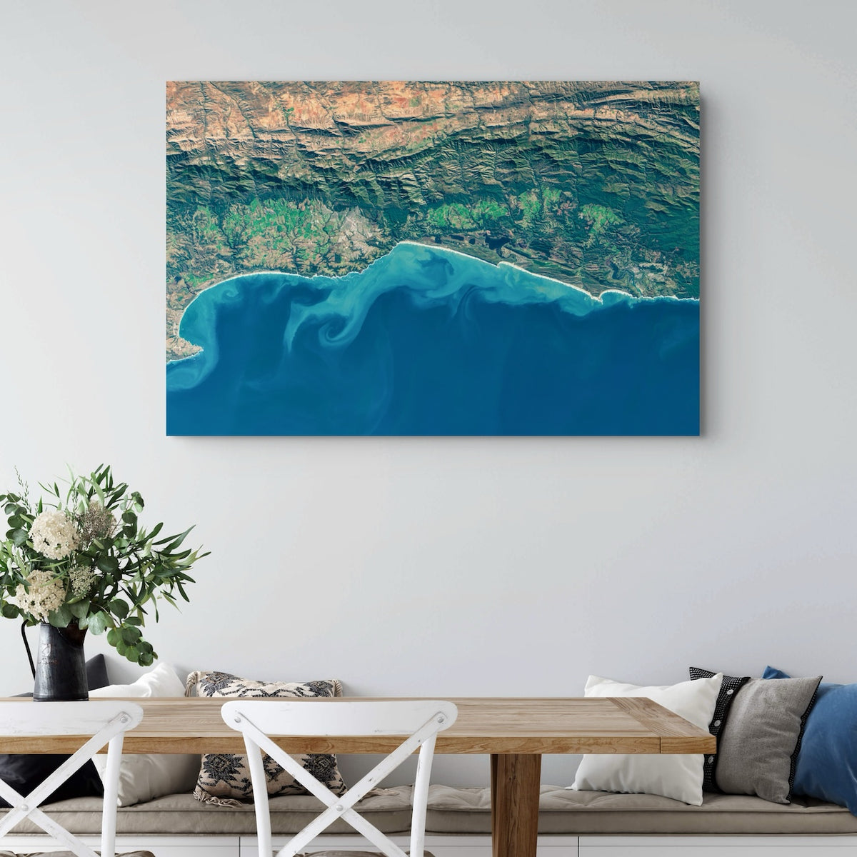 Garden Route 2 West satellite print hung on a white wall above a dining table, showing the coast with the Little Karoo beyond the Outeniqua Mountains.