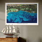 Framed artwork of a blue satellite image titled 'Garden Route' on a wall above a wooden cabinet with a ship model.