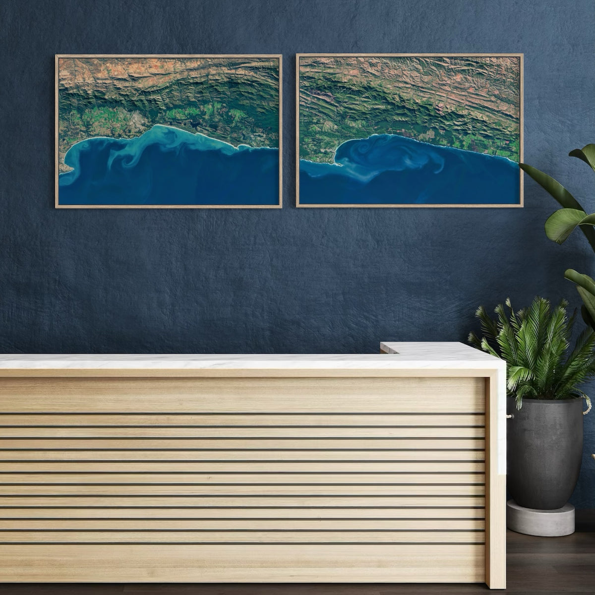 Pair of Garden Route satellite prints — Garden Route 2 West and East — framed side by side on a dark blue wall above a reception desk.
